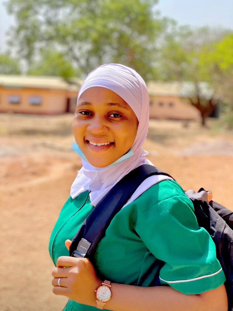 A smiling Ghanaian student nurse in uniform on her way to school